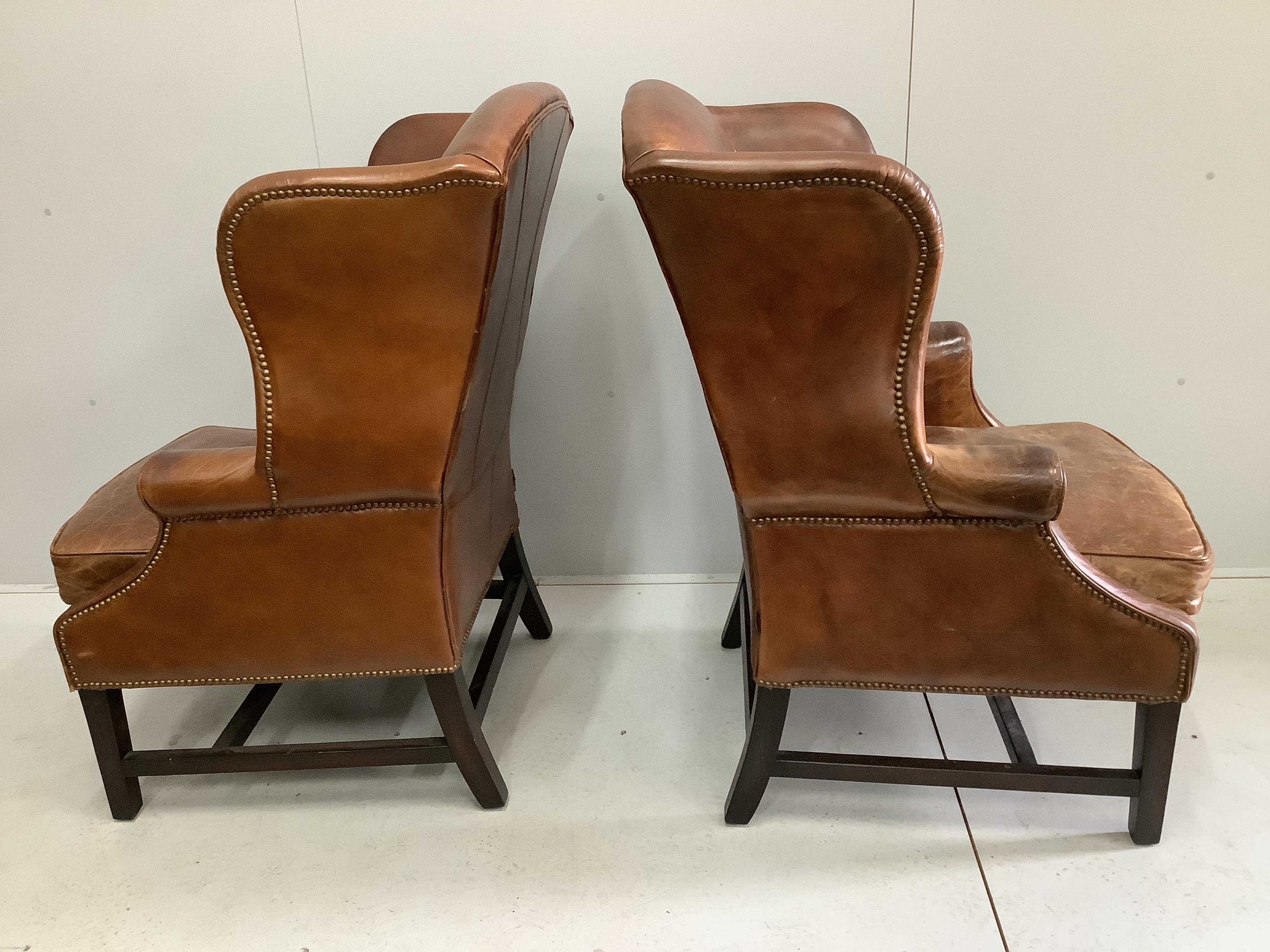 A pair of George III style studded tan leather wing armchairs, width 74cm, depth 84cm, height 112cm